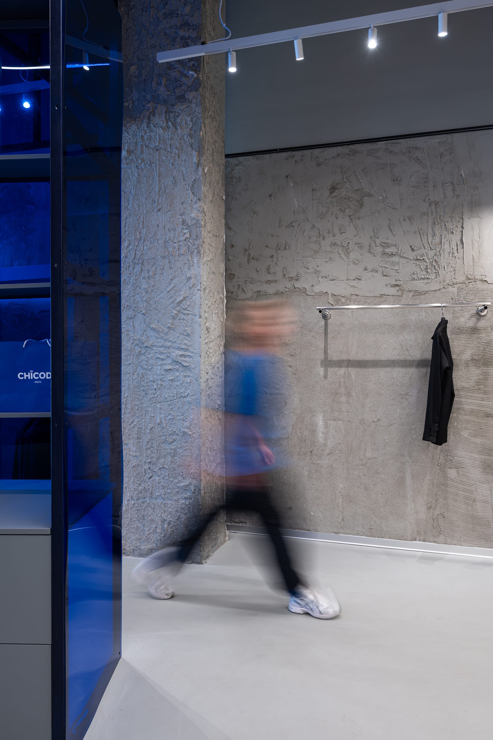 A customer walking past the raw concrete column and CHICODE branded blue glass panel