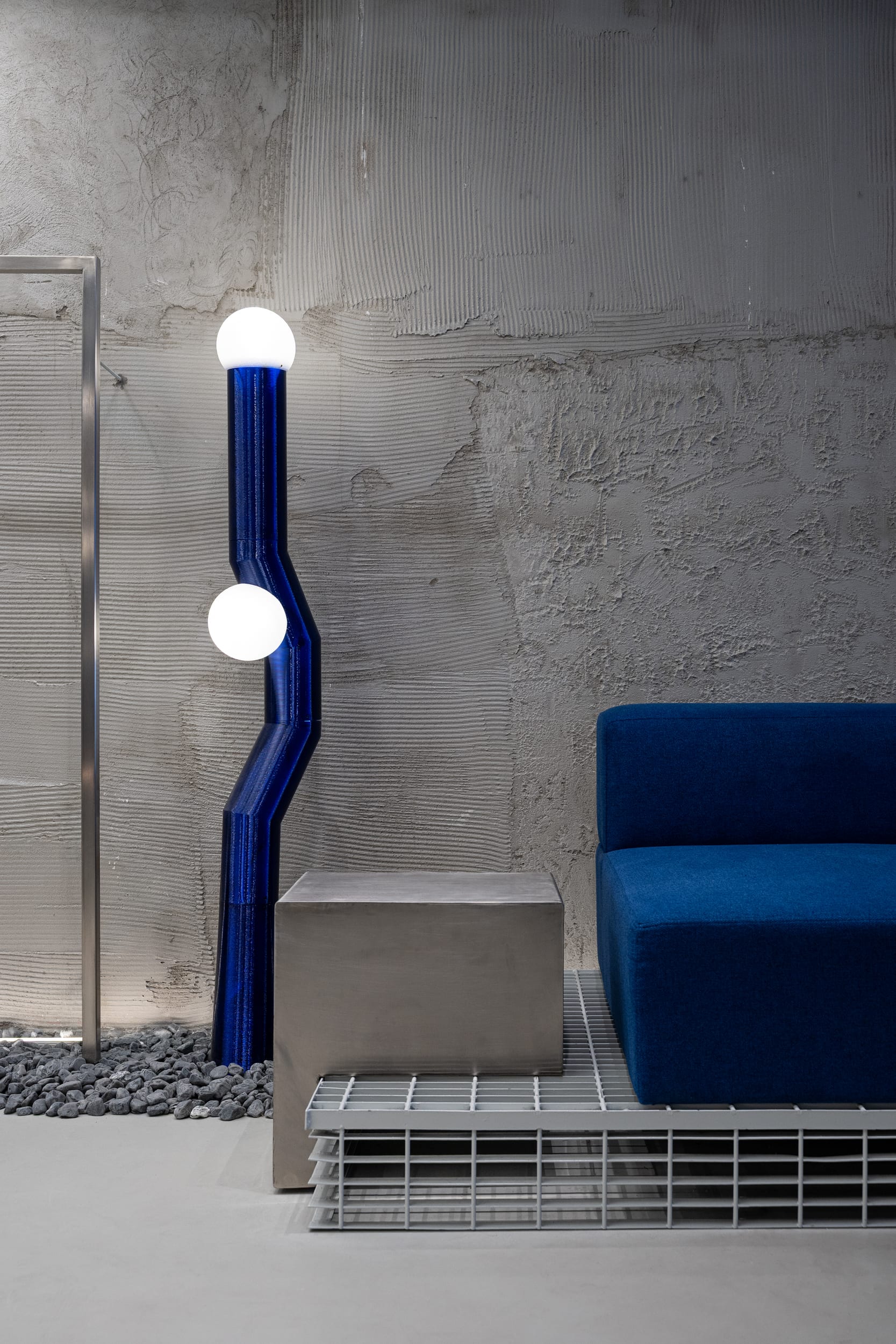 Custom 3D-printed blue floor lamp beside a steel plinth and blue velvet bench