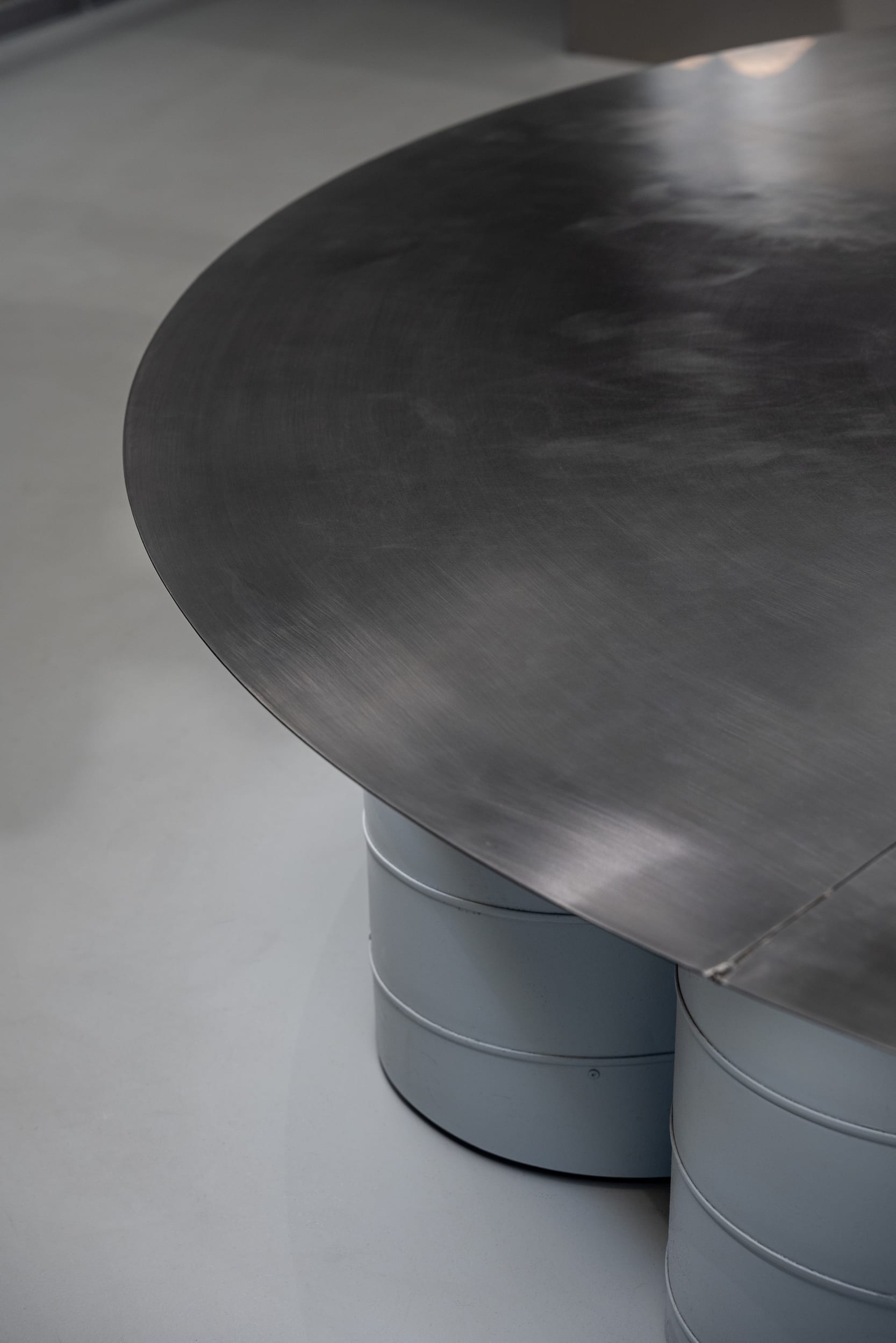 Detail of the blackened-steel display table edge on cylindrical drum legs